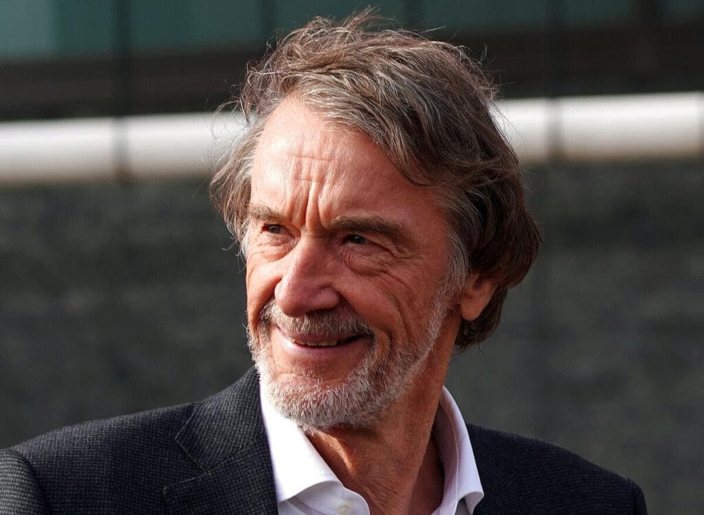 Sir Jim Radcliffe, coproprietário do Manchester United Football Club, vestindo jaqueta preta e camisa branca, com barba e bigode e penteado repartido, olhando para a esquerda