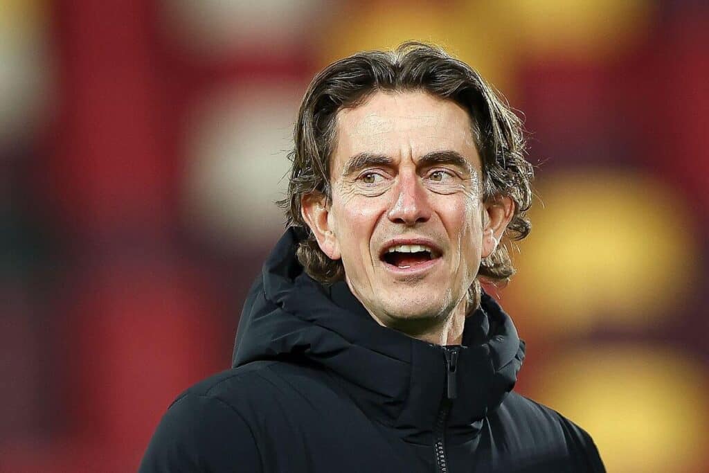 Thomas Frank, manager of Tottenham Hotspur Football Club, looks to his side and opens his mouth while wearing a black coat