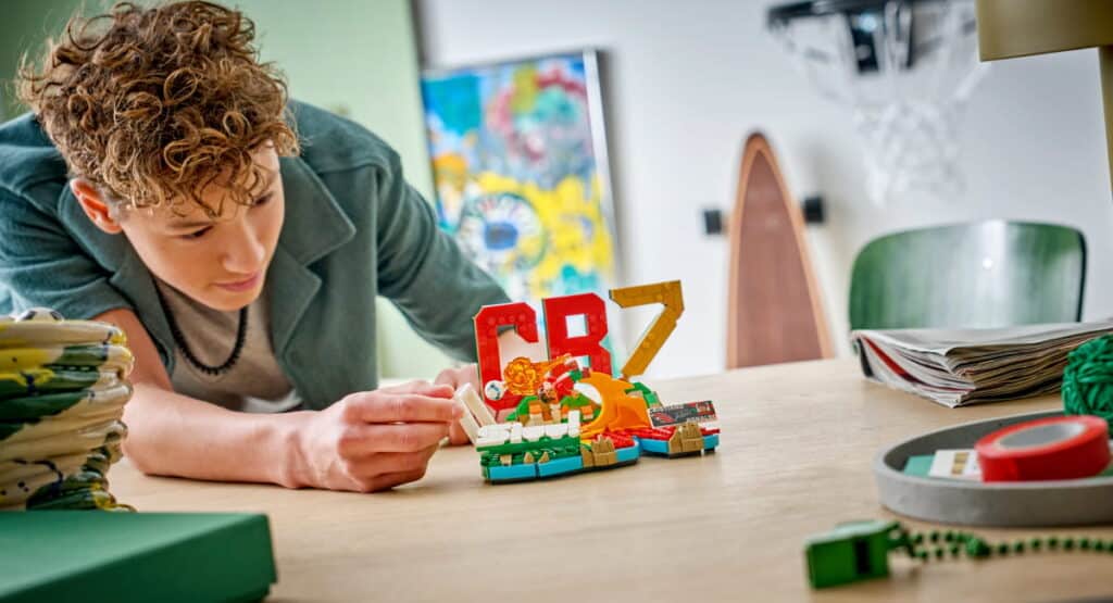 Young designer working with Lego toy at table. The designer wears a black top and touches the toy with one hand
