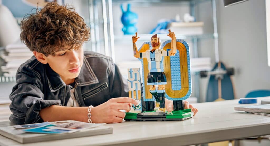 Young designer working with Lego toy at table. The designer wears a black top and touches the toy with one hand