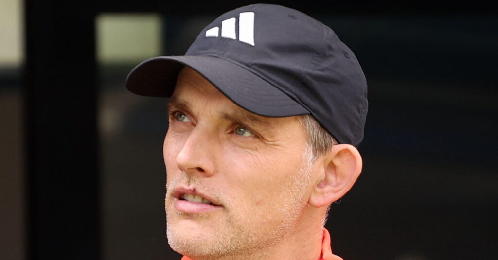 Football manager Thomas Tuchel looking upwards to his right in an outdoor setting with his mouth open while wearing a dark baseball cap with a white Adidas logo on the front