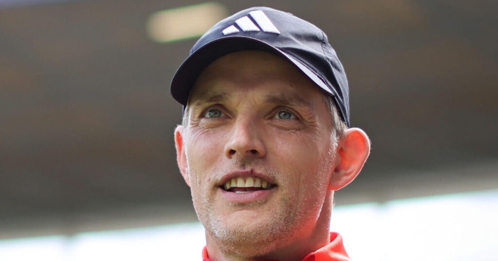 O técnico de futebol Thomas Duchel olha para o exterior, usando um boné de beisebol escuro com um logotipo branco da adidas na frente e sorrindo com a boca aberta.