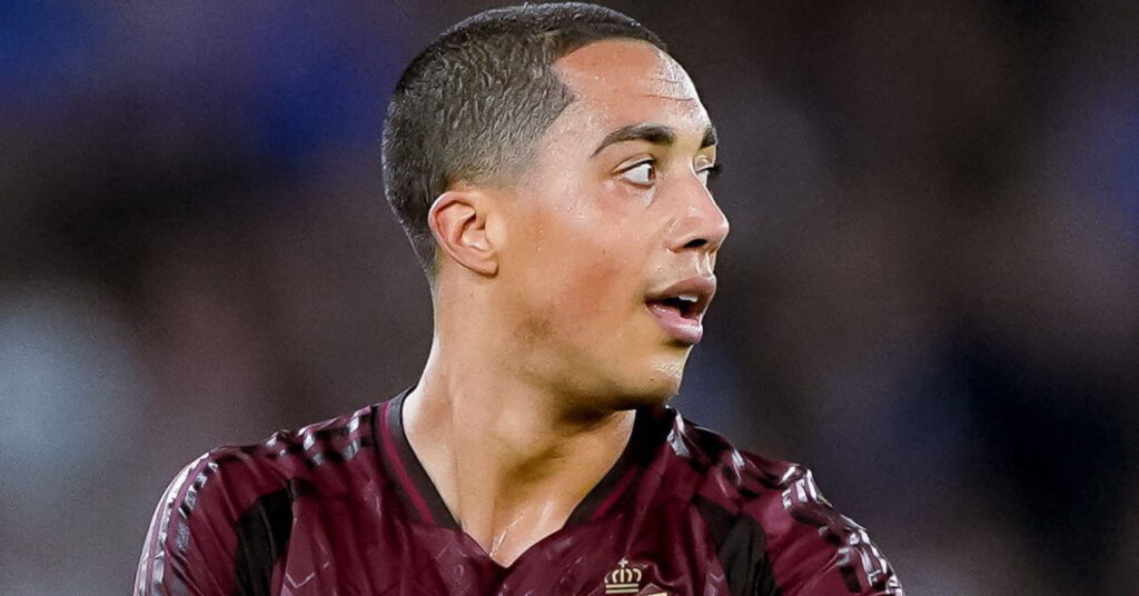Foto de youri Tielemans, um jogador de futebol com camisa marrom e jogando pela seleção belga de futebol, parado em campo e olhando para a esquerda