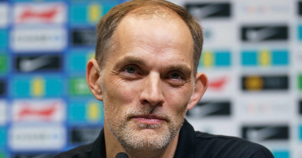 O técnico de futebol Thomas Tuchel olha para cima e sorri com um top escuro em uma entrevista coletiva
