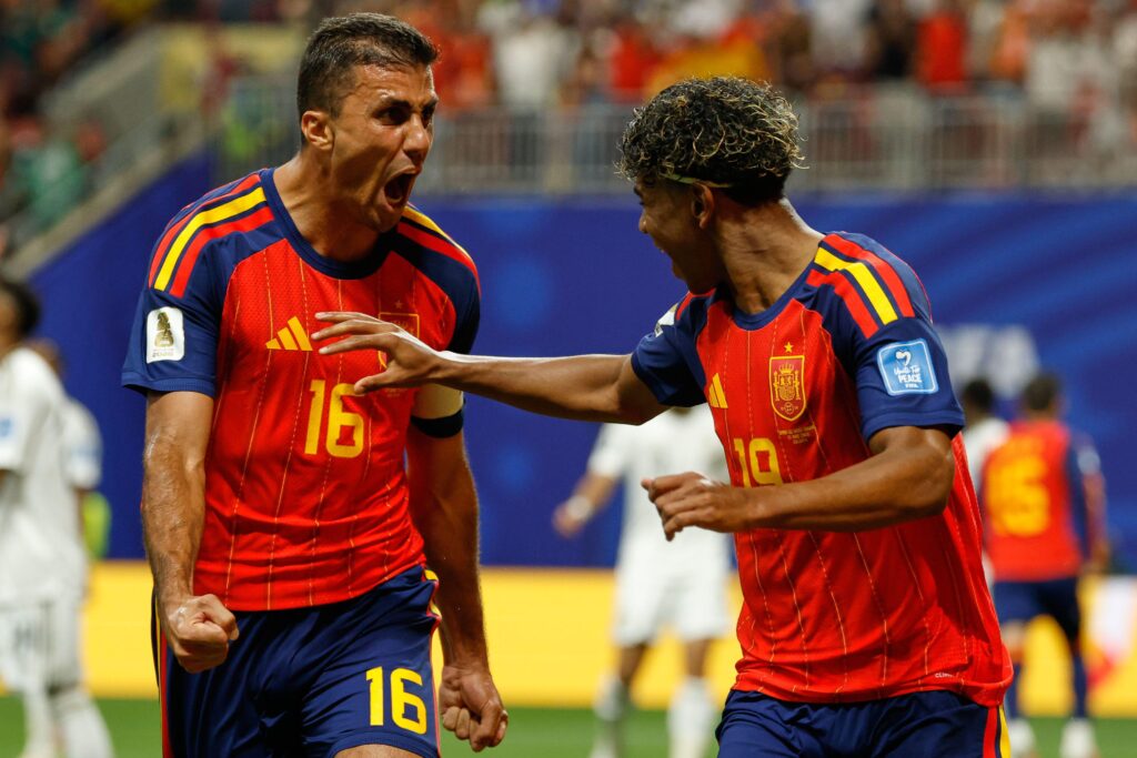 Spain footballers Rodri, who is roaring, and Lamine Yamal, who is raising his right hand and smiling, celebrating a goal while on a football pitch during the FIFA football World Cup 2026 wearing the national team shirt of red with yellow and blue