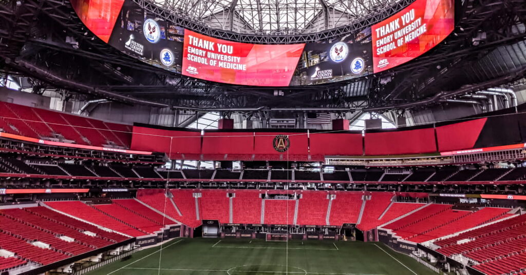 Dentro do Estádio Mercedes-Benz, sede da Copa do Mundo de 2026 e sede do Atlanta Falcons, time da NFL, e do Atlanta United FC, clube da MLS, com campo de grama verde e assentos vermelhos