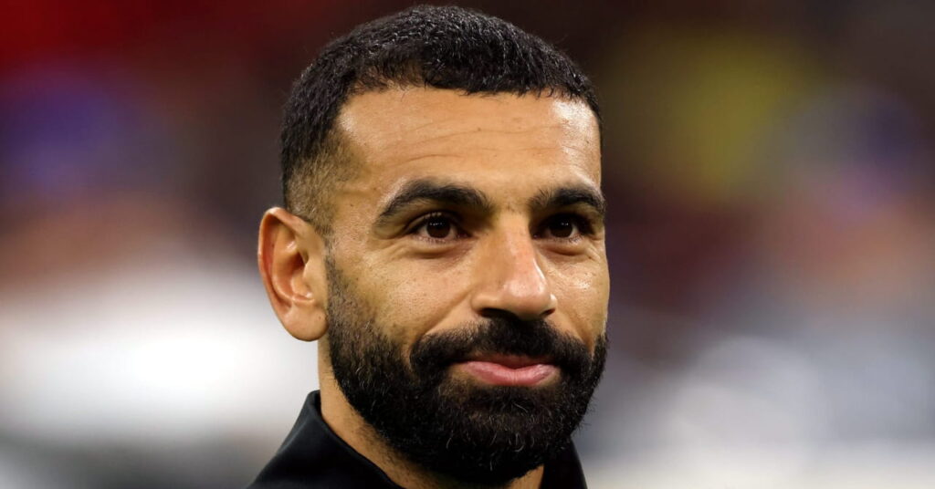 A photo of Egypt footballer Mohamed Salah looking to his left and smiling while standing on a football pitch