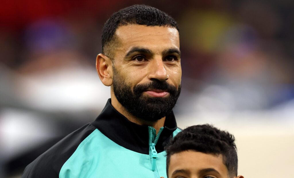 A photo of Egypt footballer Mohamed Salah looking to his left and smiling while standing on a football pitch