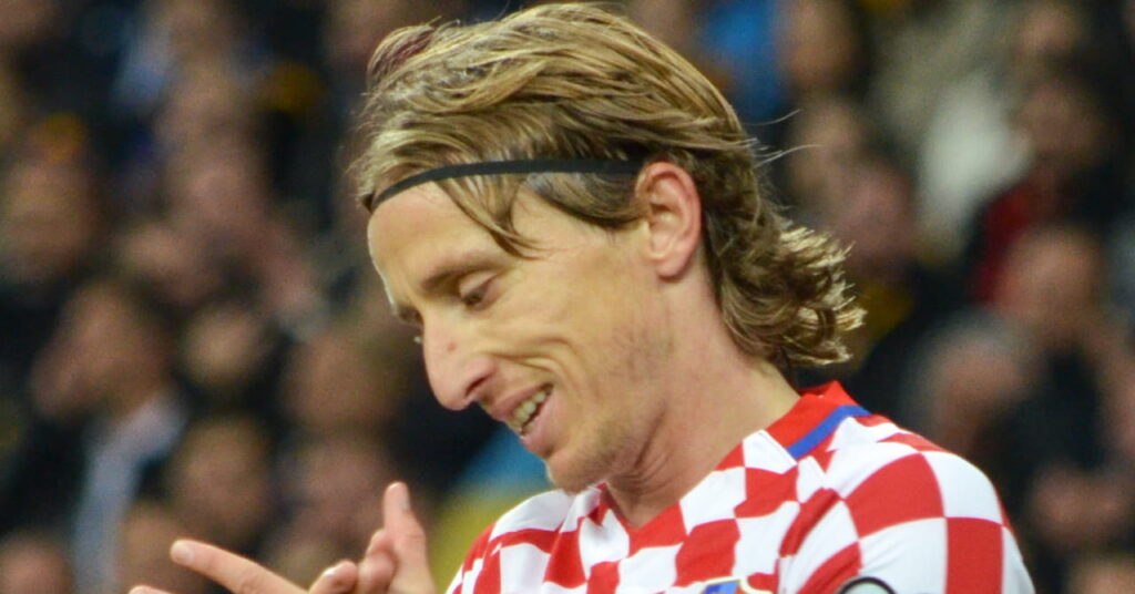 O jogador de futebol Luka Modric olha para baixo e aplaude durante o jogo com a camisa vermelha e branca da seleção croata de futebol dentro do estádio