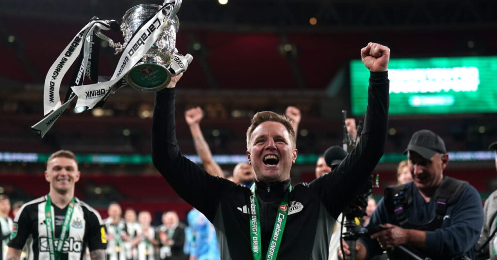 Football manager Eddie Howe holding the EFL Cup trophy and raising both arms in celebration at Wembley Stadium while wearing a black and white top when he won the Carabao Cup as head coach of Premier League club Newcastle United