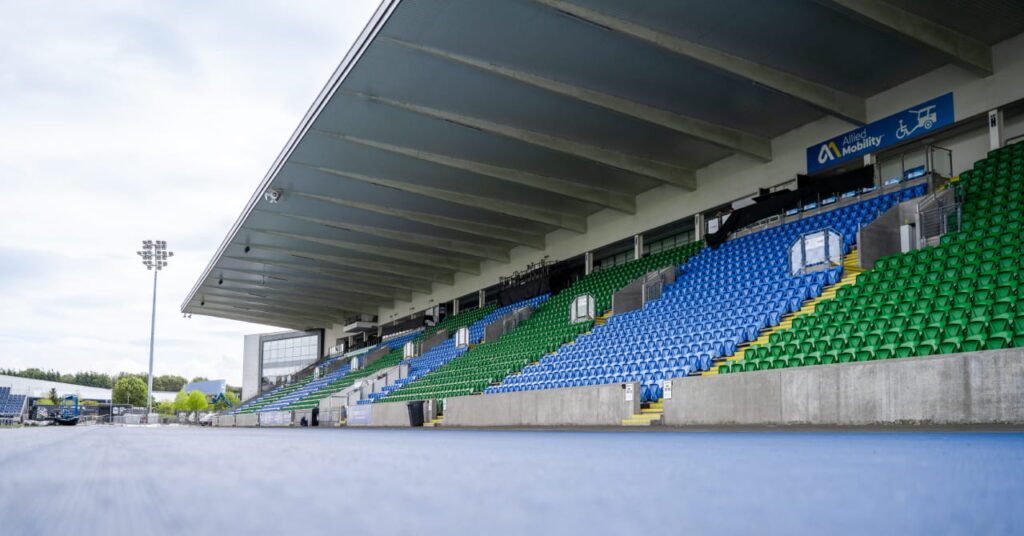 A pista e os assentos azuis e verdes para os espectadores são visíveis em frente ao local dos Jogos da Commonwealth de 2026, Scotstown Stadium.