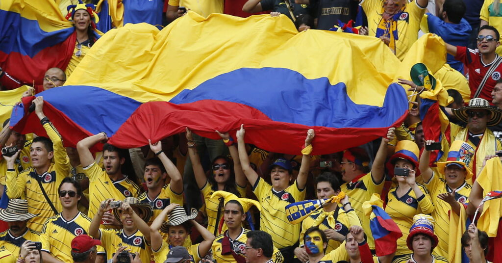 Colombia fans supporting the national football team in a stadium wearing the team colours of predominantly yellow with blue, red and white details