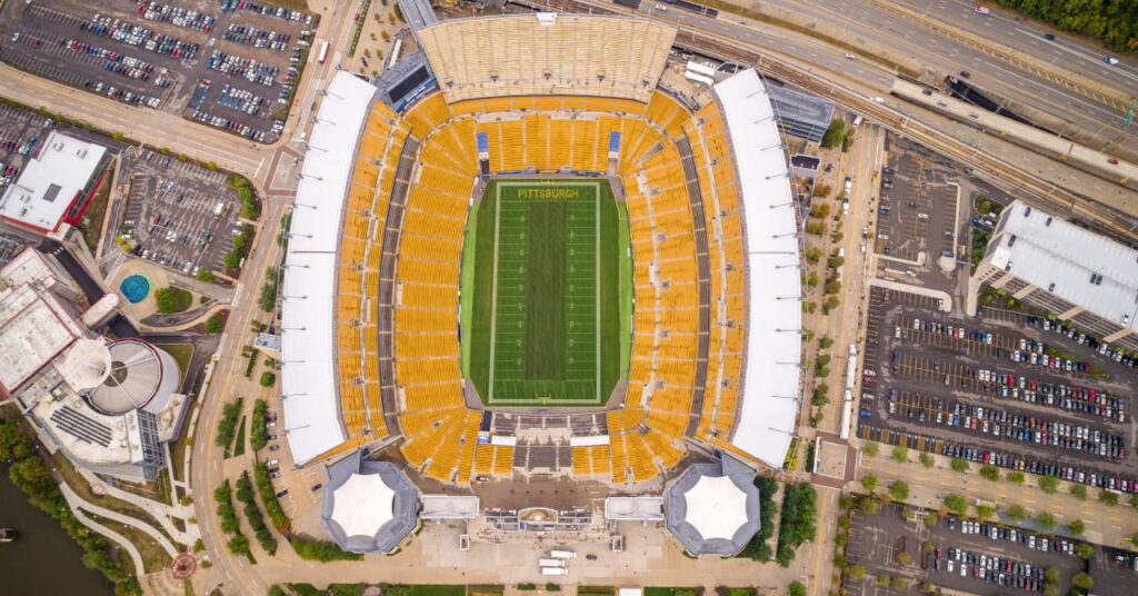 Uma foto aérea do Pittsburgh Steelers é a casa do time de futebol americano da NFL, o Pittsburgh Steelers 'Acrisar Stadium, anteriormente conhecido como Heinz Field, e é mostrada com assentos amarelos ao redor do campo verde ao redor da estrada.