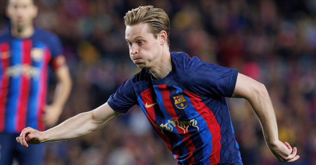 Netherlands footballer Frenkie de Jong playing for La Liga team Barcelona Football Club in a blue and red striped top while shifting a ball forward on a pitch, puffing out his cheeks and wearing white boots