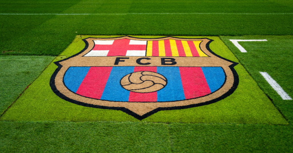 Lo stadio Camp Nou, sede della squadra della Liga, il Barcelona Football Club, alla luce del giorno, con un campo verde e l'emblema dello stemma rosso, blu e giallo del club contrassegnato
