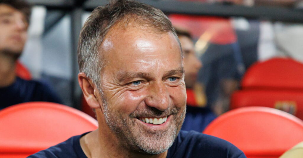 Football manager Hansi Flick looking to his left on a red seat in a stadium in his role as manager of La Liga side Barcelona Football Club