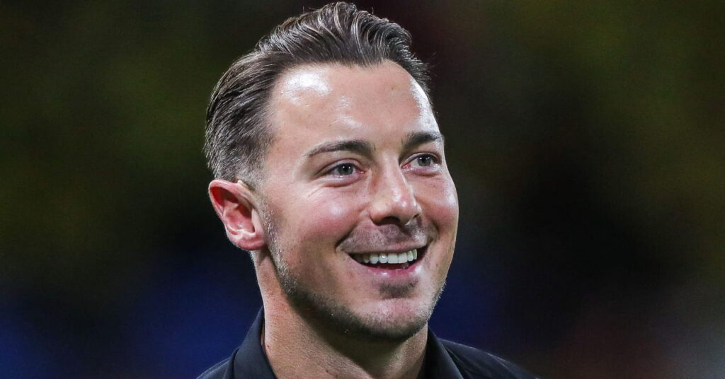 Manager Matthias Jaissle looking to his left and smiling while wearing a dark shirt in a stadium as head coach of Premier League team Newcastle United Football Club