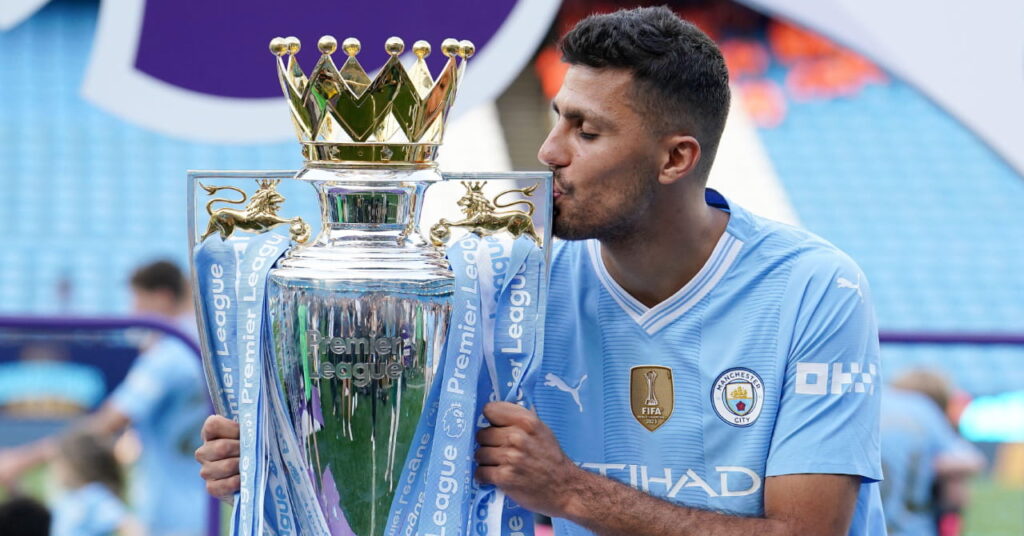 Spain footballer Rodri kissing the silver and gold Premier League trophy in a stadium while playing for team Manchester City Football Club in a light blue shirt