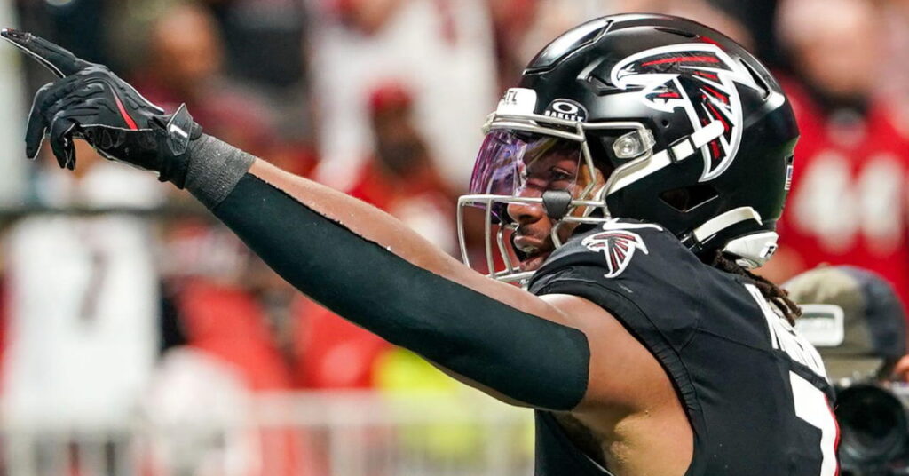 American footballer Bijan Robinson raising his left hand while wearing the predominantly black shirt and helmet of NFL American football team the Atlanta Falcons in a stadium