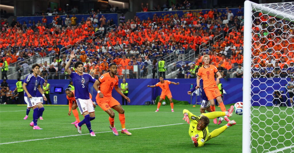 Footballer Zion Suzuki making a save while playing football for the Japan national team against the Netherlands at the World Cup 2026 and wearing a yellow kit with black trim with salmon gloves and boots playing with a white ball