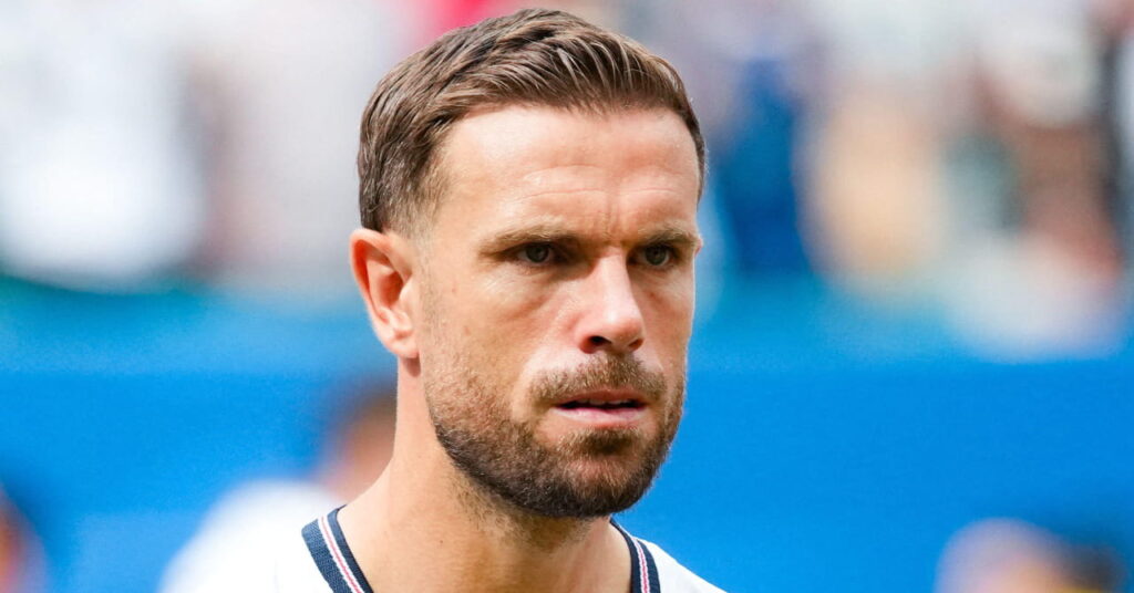 England footballer Jordan Henderson looking to his left while playing international football in a white shirt with blue trim and his number 14 in red on the chest while wearing a cast on his left arm