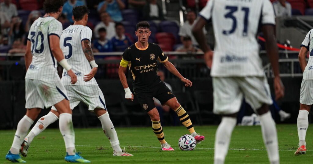 Il calciatore del Manchester City Phil Foden ha la palla ai suoi piedi con la divisa nera e gialla mentre affronta i giocatori dell'Inter in bianco su un campo verde durante una partita del Manchester City Football Club