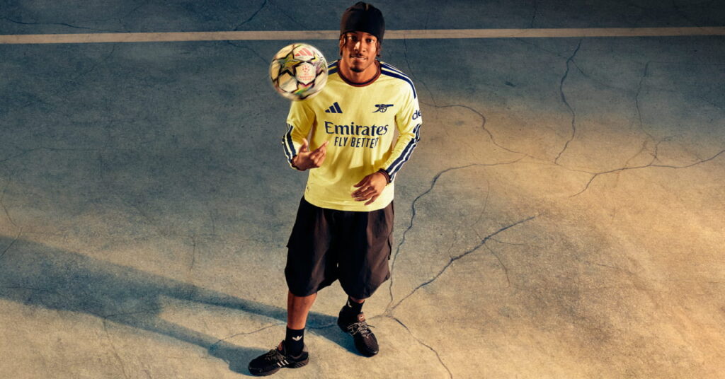 Footballers Eberechi Eze standing in a shadowy room in the third kit of Premier League team Arsenal Football Club which is coloured yellow with blue trim