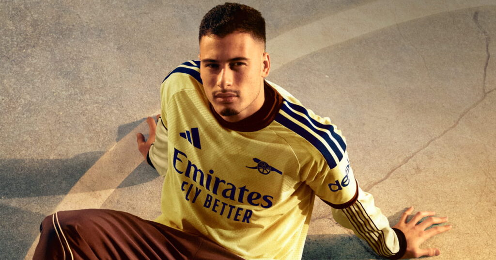 Brazil footballer Gabriel Martinelli standing in a shadowy room in the third kit of Premier League team Arsenal Football Club which is coloured yellow with blue trim