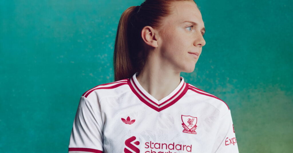 Footballer Ceri Holland wearing the Adidas Liverpool Football Club Premier League away hoodie of white with red trim