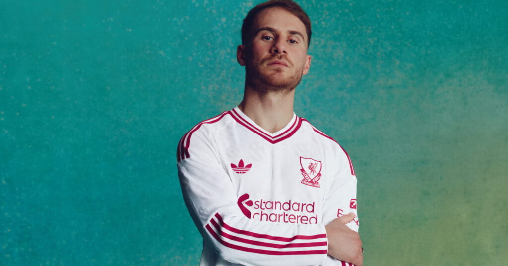 Footballer Alexis Mac Allister wearing the Adidas Liverpool Football Club Premier League away hoodie of white with red trim
