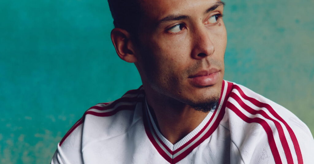 Footballer Virgil van Dijk looking to his left while wearing the Adidas Liverpool Football Club Premier League away kit of white with red trim
