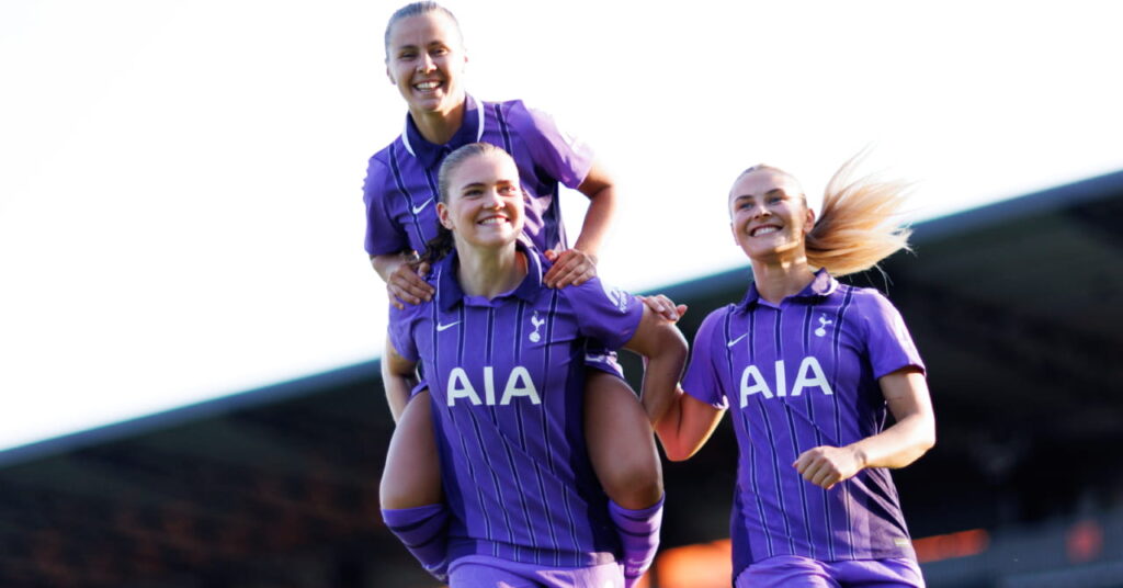 Footballers Victoria Pelova, Signe Gaupset and Amanda Nilden celebrating a goal on a pitch while wearing the purple third shirt of Premier League team Tottenham Hotspur Football Club