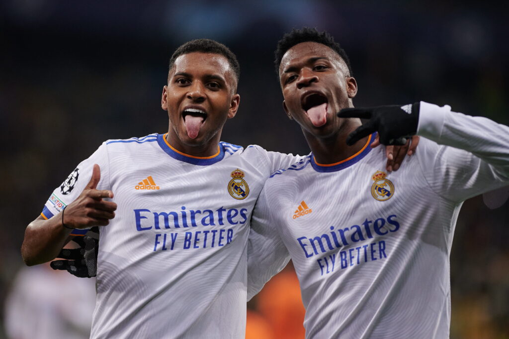 O jogador de futebol Vinicius Junior comemora um gol mostrando a língua e colocando dois dedos enluvados da mão esquerda no rosto enquanto joga pelo Real Madrid, clube de futebol da La Liga