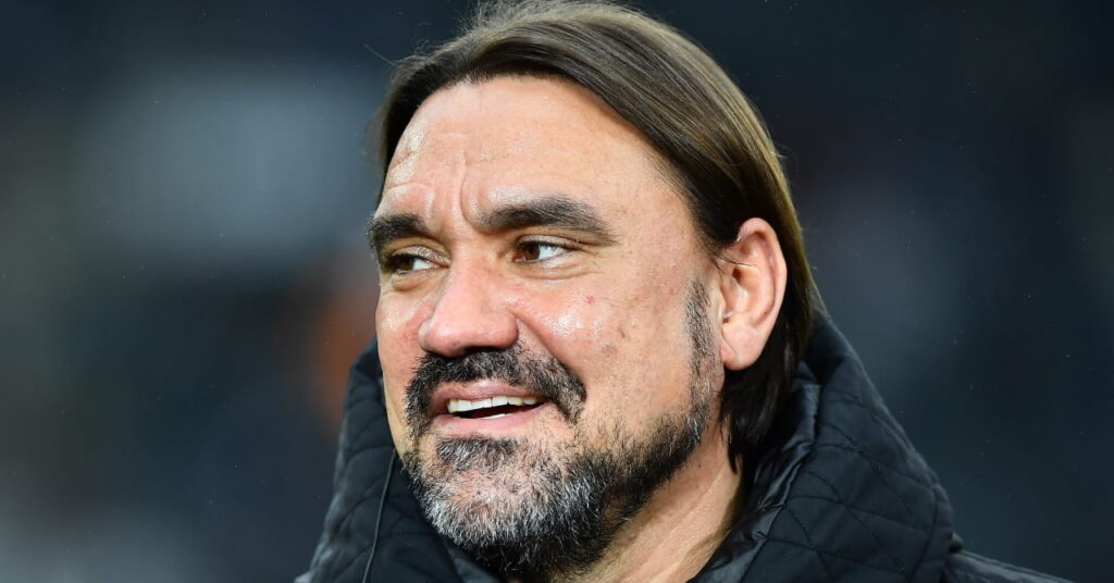 O técnico Daniel Farke olha para a direita e sorri enquanto veste um casaco preto em campo como técnico do Leeds United Football Club, da Premier League.