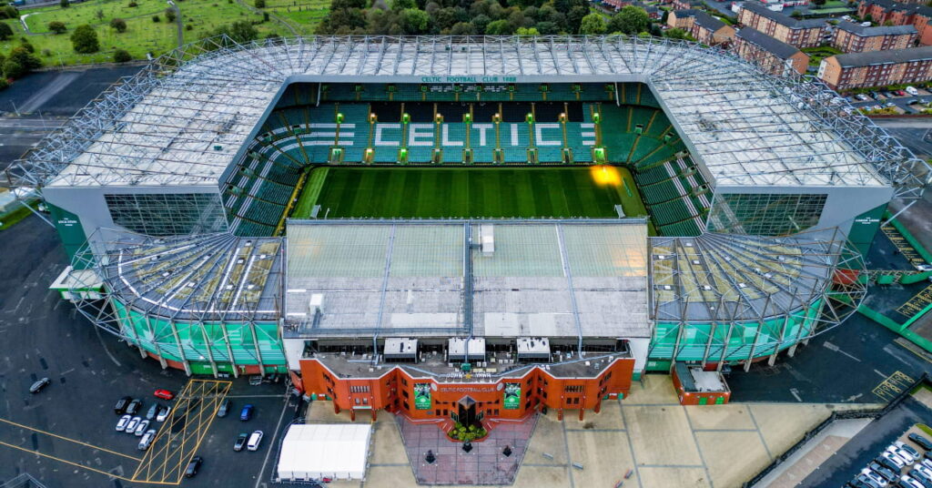 An overhead view of the Celtic Park stadium home of The green and white striped badge of Scottish Premiership team Celtic Football Club showing green seats and the word Celtic spelled out in white and the surrounding residential neighbourhood and streets in Glasgow