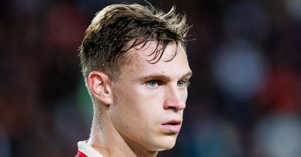 Germany footballer Joshua Kimmich looking to his left on a pitch while playing for Bundesliga football club Bayern Munich in a white shirt with red trim