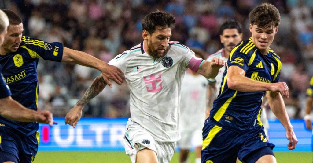 Il calciatore argentino Lionel Messi si allontana dai giocatori dell'opposizione mentre gioca per la squadra di calcio della Major League Inter Miami in una divisa bianca con divisa nera, rosa e azzurra contro avversari in divisa blu scuro e gialla nella MLS