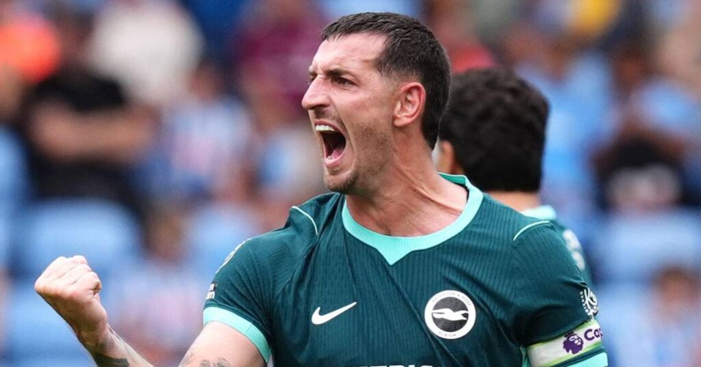 O jogador de futebol Lewis Dunk levanta o punho direito e ruge para comemorar um gol enquanto joga pelo Brighton and Hove Albion Football Club, da Premier League, com uma camisa verde com o emblema do clube e o logotipo da Nike na camisa