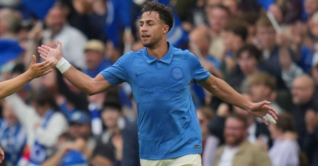 O jogador de futebol grego Charalambos Kostoulos, que joga no Brighton and Hove Albion Football Club, da Premier League, comemora um gol com o braço direito levantado.