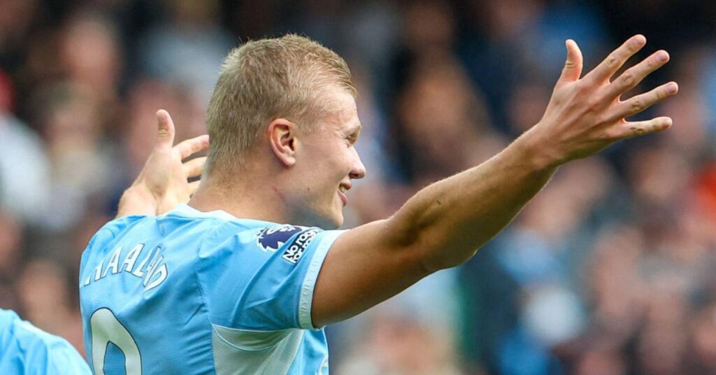 Norway footballer Erling Haaland raising his arms in celebration and smiling while looking to his left and playing for Premier League team Manchester City Football Club in a light blue and white shirt with his surname and number nine on the back in white