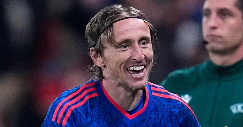 O jogador de futebol do AC Milan, Luka Modric, sorri para comemorar um gol com uma camisa azul com detalhes adidas nos ombros e no pescoço da seleção croata de futebol.