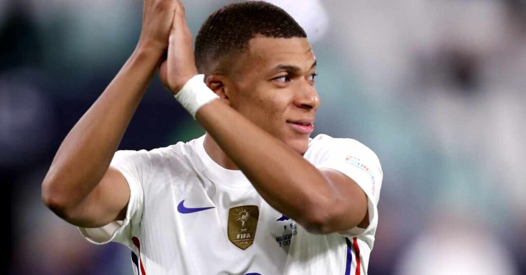 Kylian Mbappe, jogador de futebol do Real Madrid Football Club, da La Liga, olha para a esquerda e aplaude, jogando pela seleção francesa com uma camisa branca e uma faixa branca no pulso esquerdo.