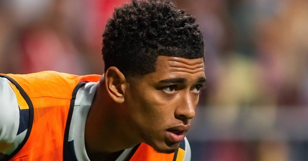 England footballer Jude Bellingham looking to his left in a stadium while playing for La Liga team Real Madrid Football Club in an orange and black bib over a white shirt with yellow and dark blue trim