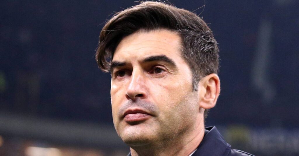 O técnico de futebol Paolo Fonseca, vestindo capa de chuva escura e camisa branca, olhando diretamente para o campo, atua como técnico do Olympique Lyonnais ou do Lyon, clube da Ligue 1.